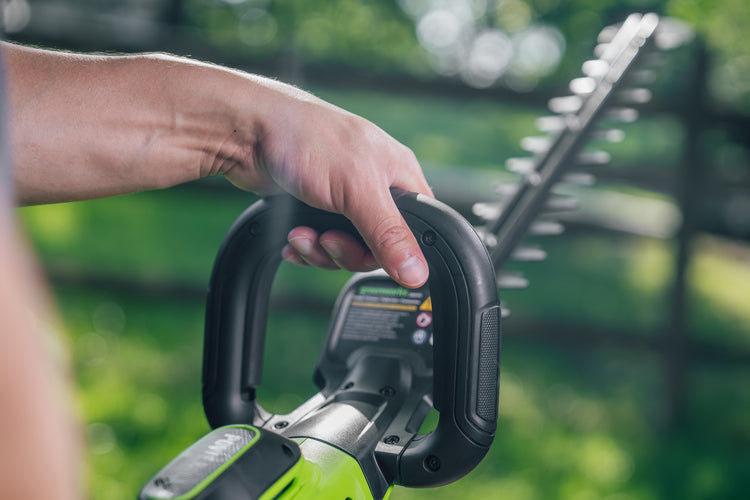 Hand holding a cordless hedge trimmer with a blurred green background