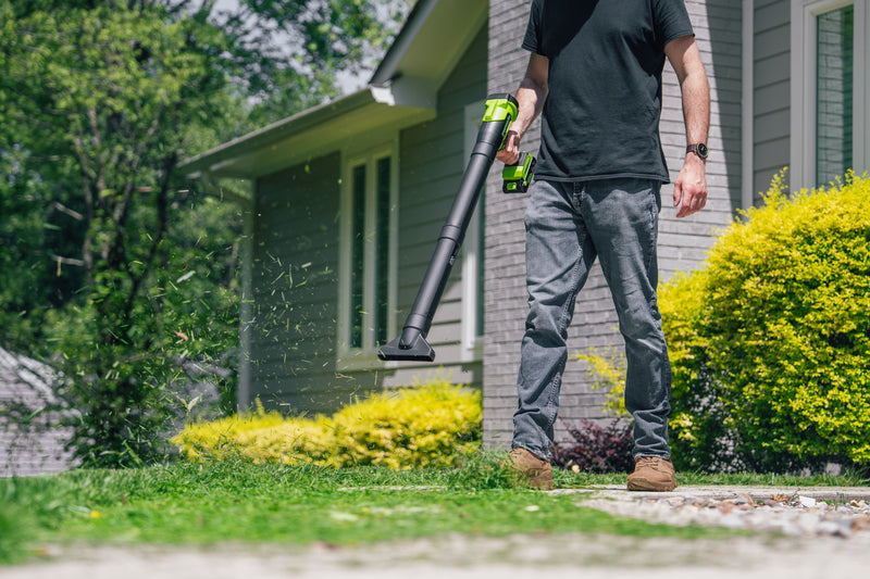 Person holding a leaf blower in front of a house with greenery