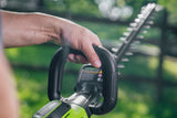 Hand holding a cordless hedge trimmer with a blurred green background