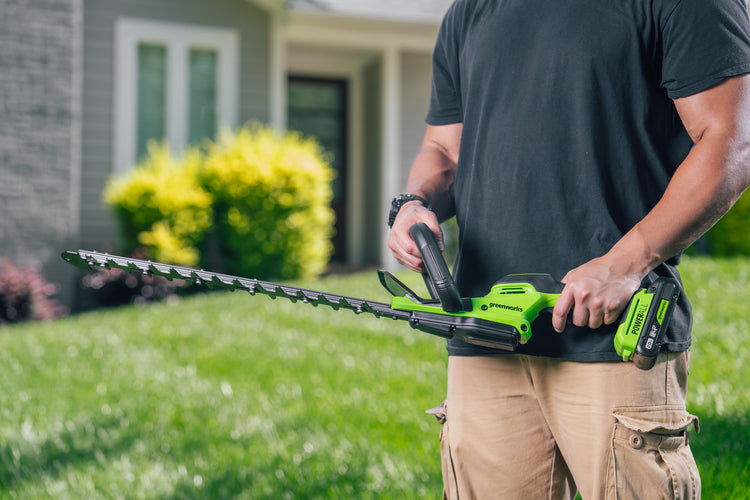 Person holding a green hedge trimmer in a grassy area