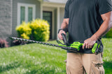 Person holding a green hedge trimmer in a grassy area